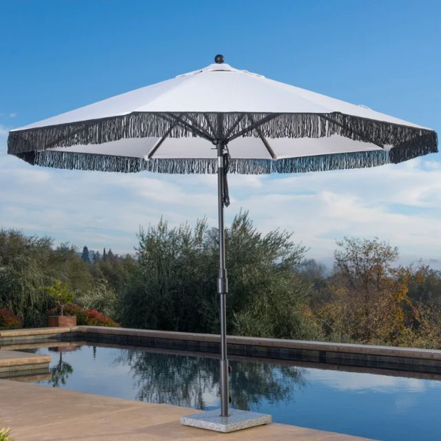 A patio umbrella near a pool in an outdoor setting with trees in the background