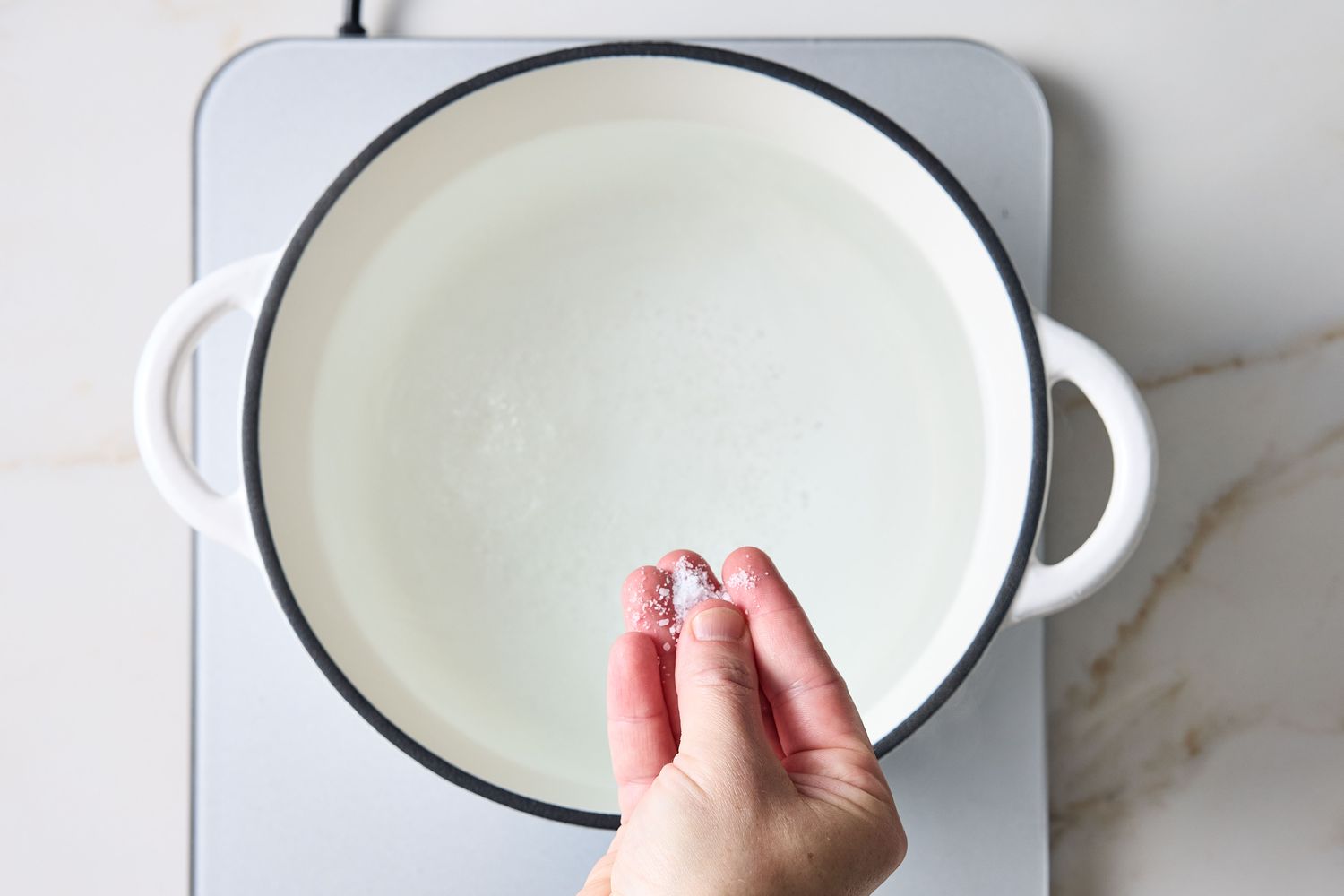 Hand sprinkling salt into a pot of water on a stove