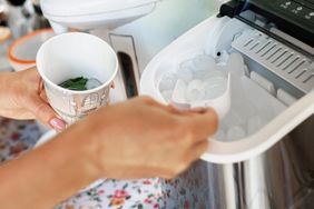A person collecting ice with a scooper from a machine and placing it into a cup