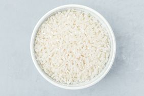 A bowl filled with uncooked white rice on a gray surface