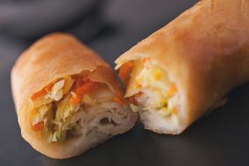 Two spring rolls one whole and one cut open to reveal filling served on a dark surface