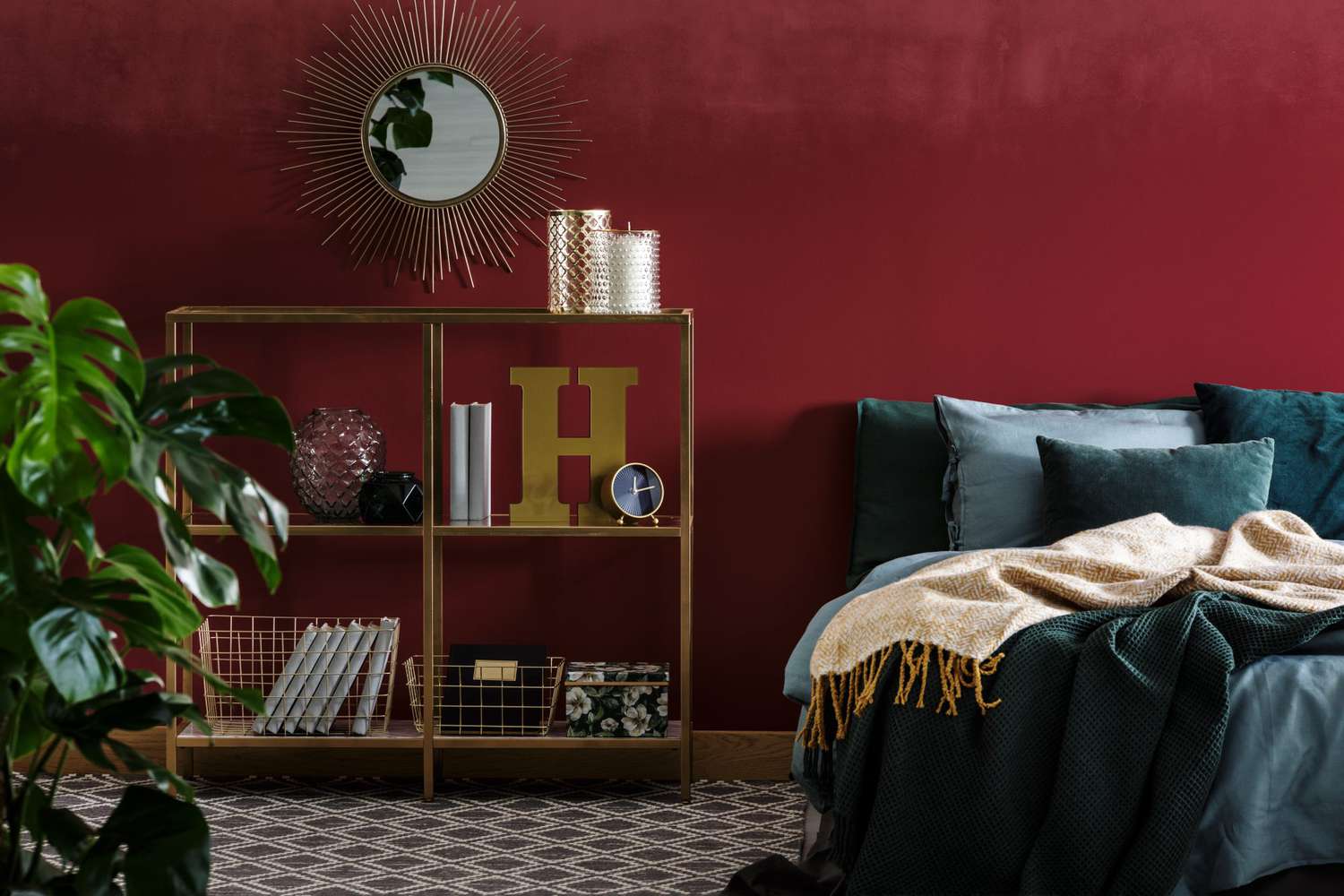 Blanket on green bed in red modern bedroom interior with gold round mirror above shelves