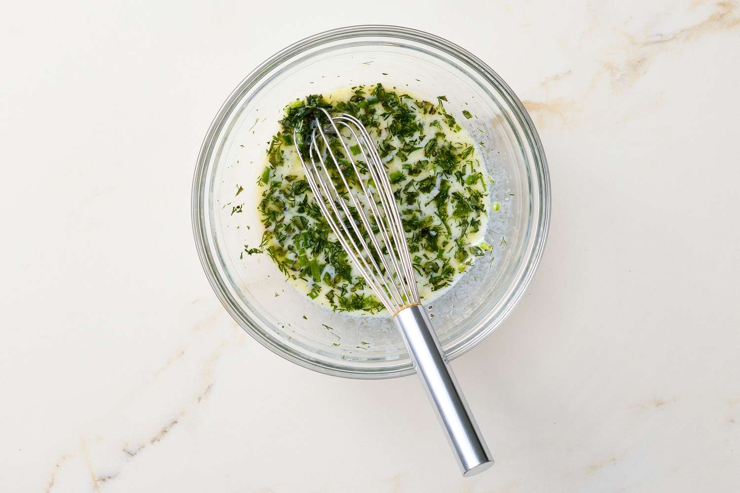 A glass bowl containing a buttermilk herb vinaigrette with a whisk