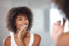 woman looking in mirror brushing teeth