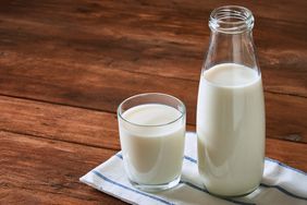 A bottle and a glass of milk on a wooden surface with a cloth
