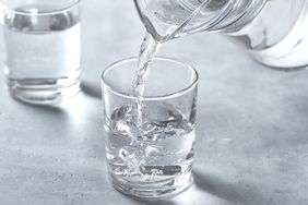 Water being poured from a pitcher into a glass with a second glass filled in the background