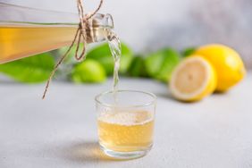 A sparkling beverage being poured into a glass with lemons and greenery in the background