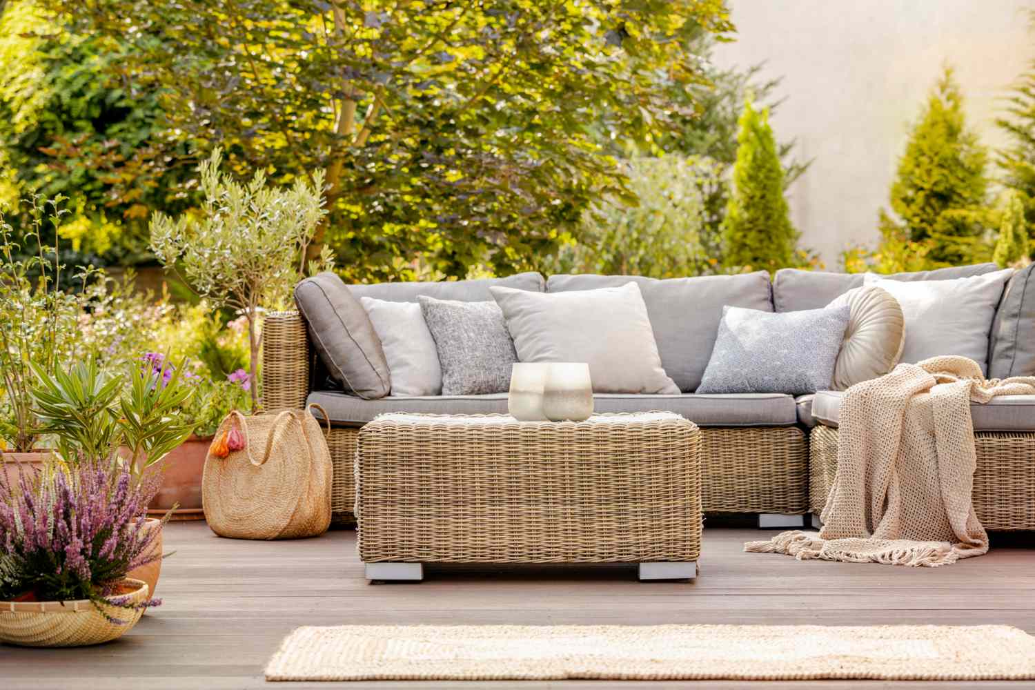 Outdoor patio with a wicker sofa cushions a woven ottoman and a cozy atmosphere surrounded by greenery and potted plants