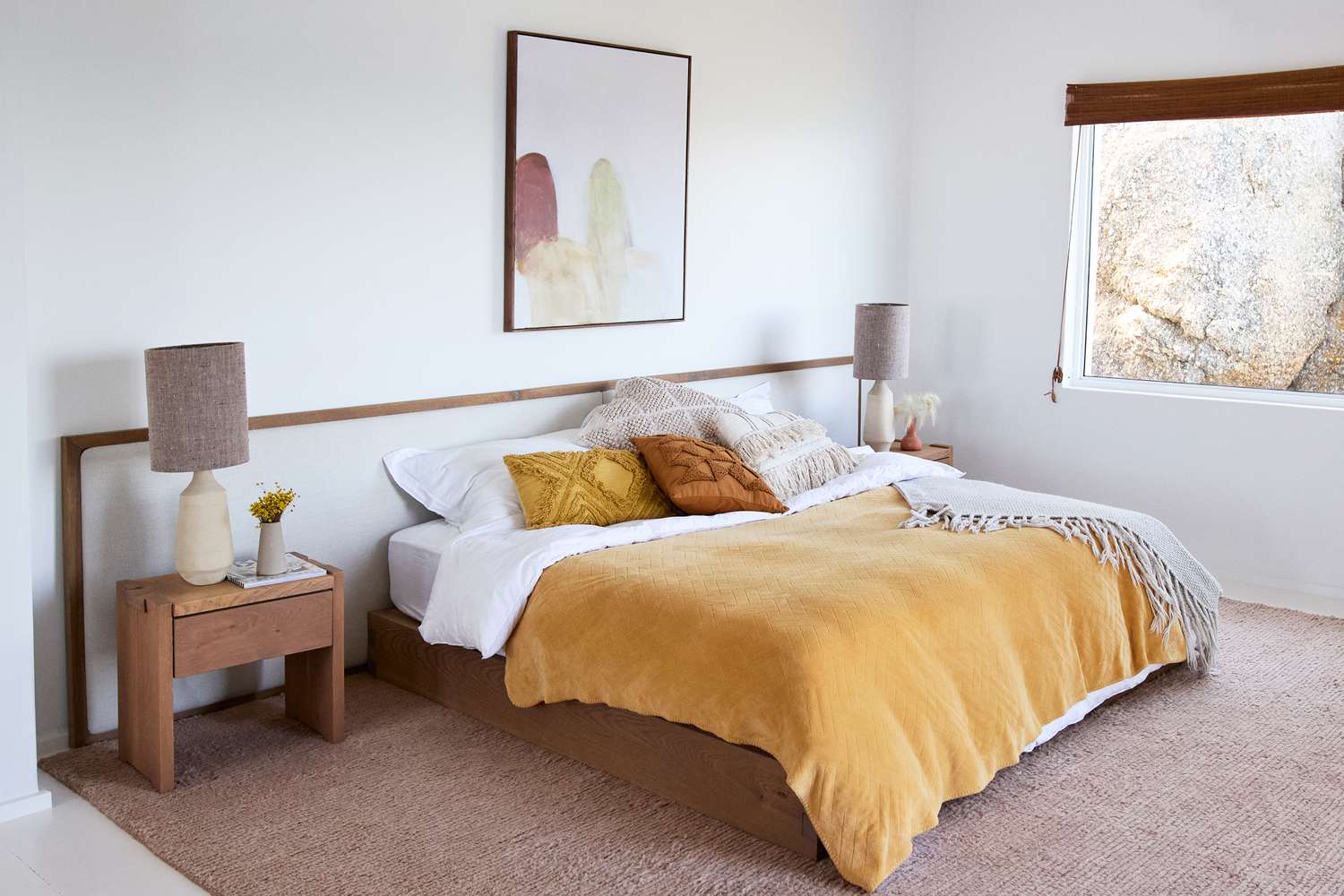 A neatly organized modern bedroom with a bed pillows and matching nightstands under a painting