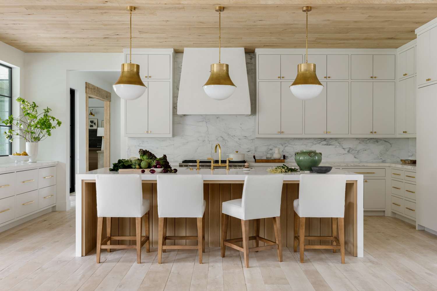 A modern kitchen featuring a white island with barstools, pendant lights, and cabinetry
