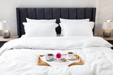 A neatly made bed with a tray holding cups saucers and a flower placed on the duvet
