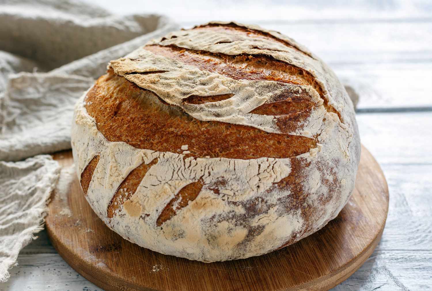 A loaf of sourdough bread on a wooden board with a cloth in the background