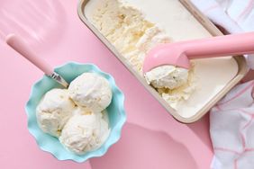 A bowl of scooped vanilla ice cream next to a tub with an ice cream scooper