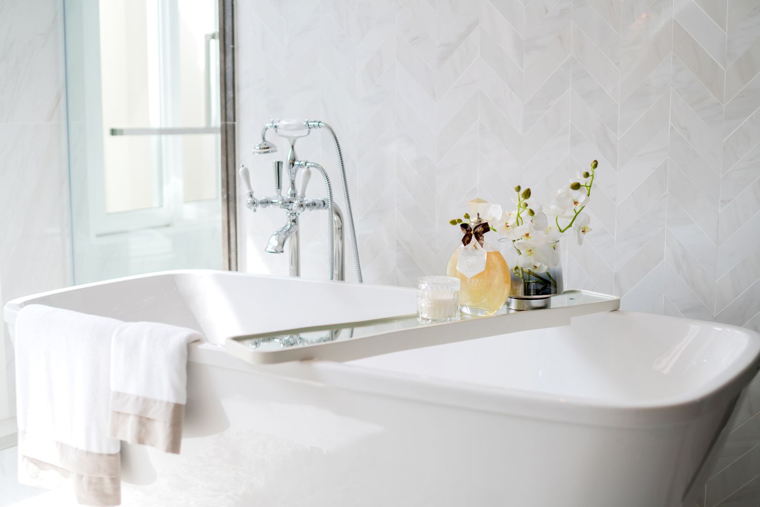 chrome faucet on white bathtub with table and towels