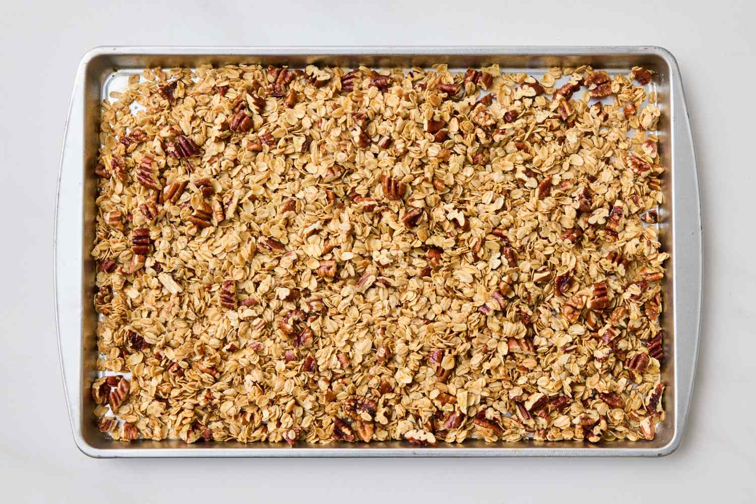 A baking tray filled with a mix of granola and pecans spread evenly across the surface