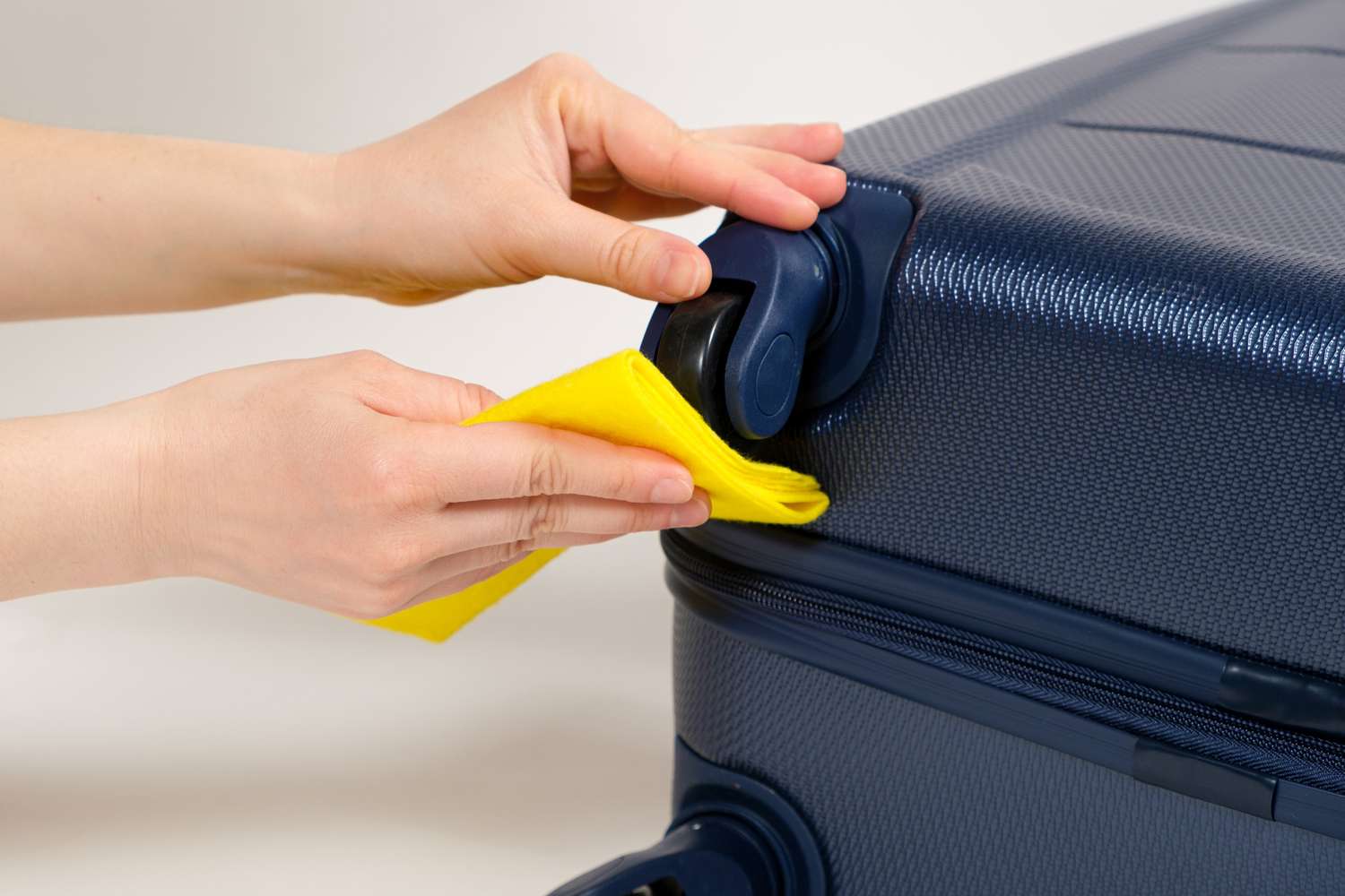 Hands cleaning a suitcase wheel with a yellow cloth