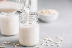 Pouring oat milk into a glass jar with oats visible in the background