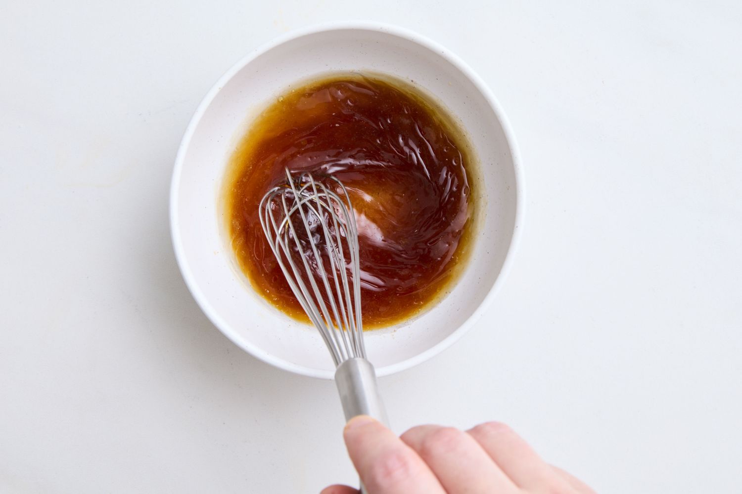 A hand whisking dressing in a white bowl preparing ingredients