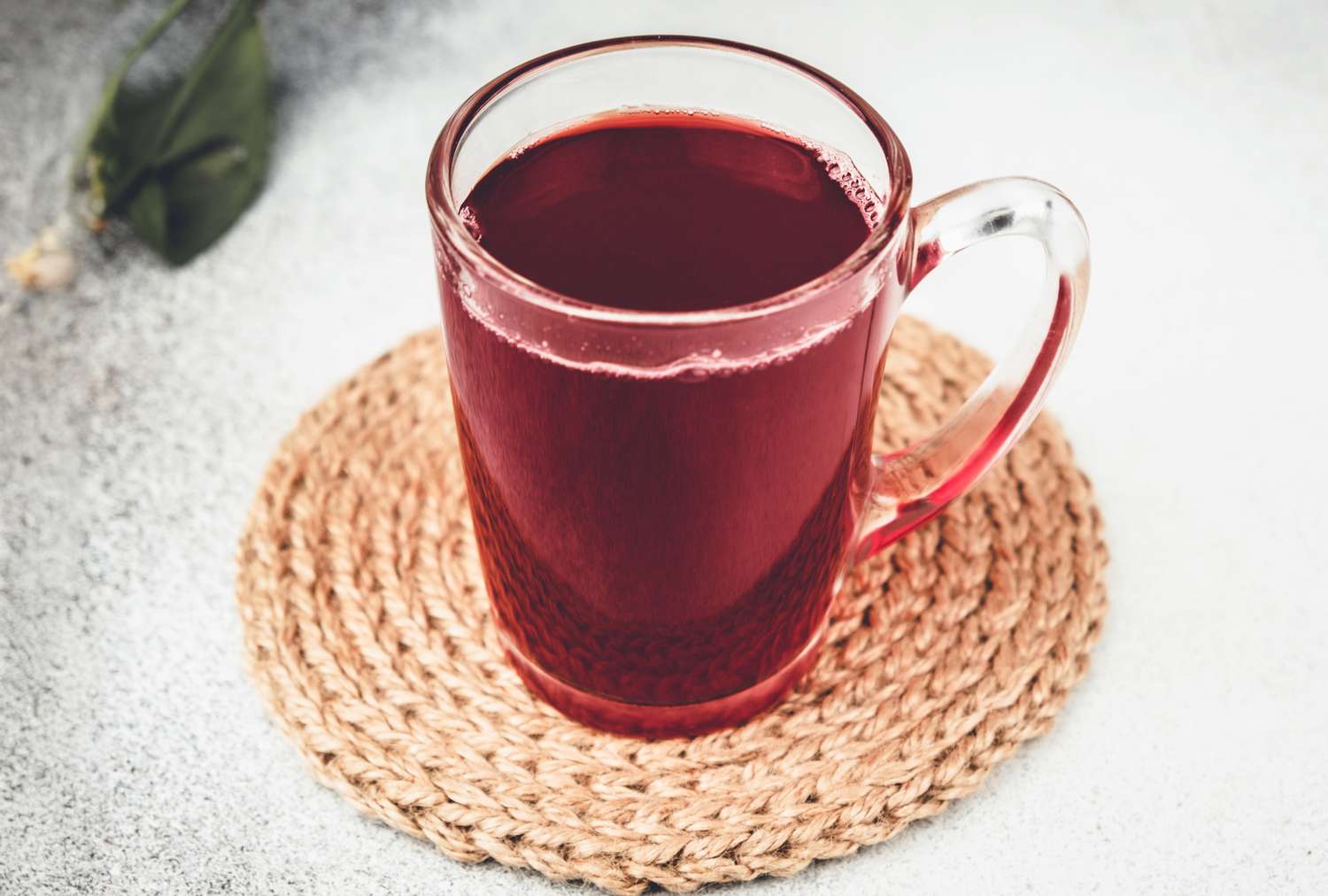 A glass mug with cherry juice resting on a woven coaster