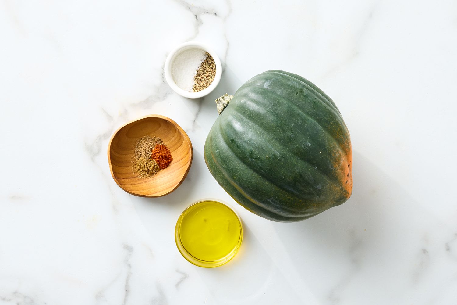 Acorn squash with small bowls of spices salt and olive oil placed on a marble surface