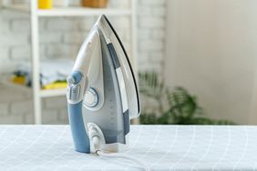 A steam iron standing on an ironing board in a home setting with blurred background objects