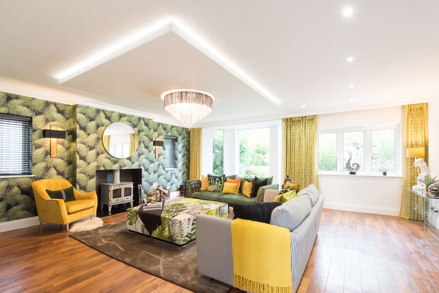 A stylishly furnished living room featuring a patterned couch yellow chair large windows and a decorative wall backdrop with a mirror