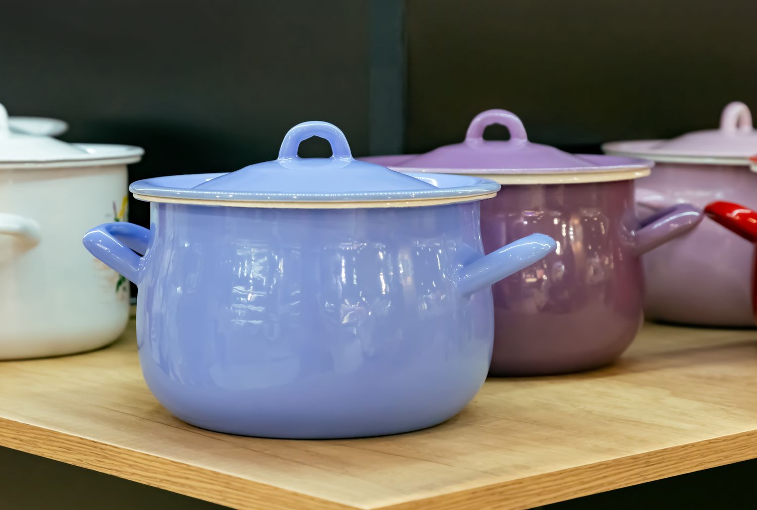 Several enamel pots with lids displayed on a wooden shelf