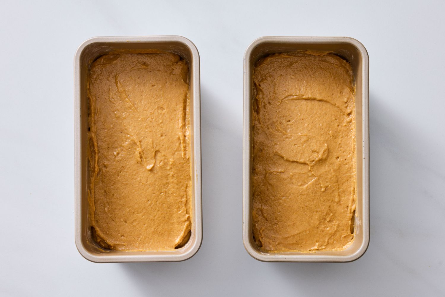 Two loaf pans filled with pumpkin batter on a white surface