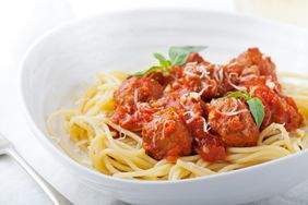 A plate of spaghetti with meatballs and tomato sauce garnished with grated cheese and fresh herbs