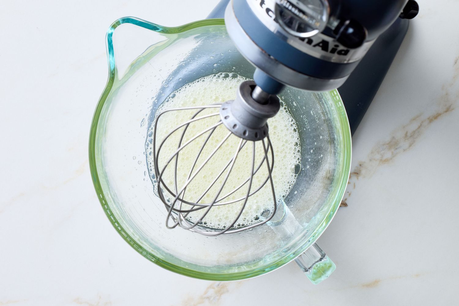 Stand mixer whisking ingredients in a glass bowl