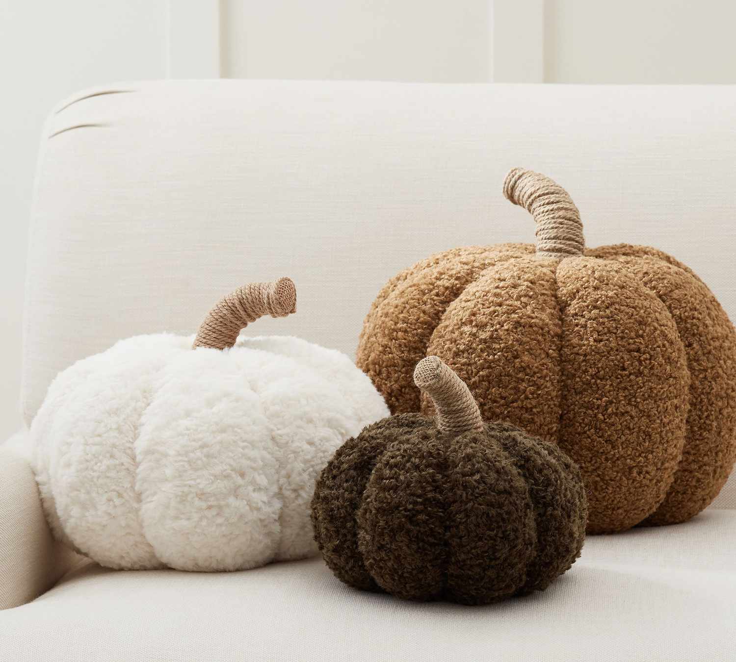 Three decorative pumpkinshaped pillows on a white surface