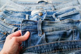Hand holding the waistband of a pair of denim jeans multiple denim garments laid out in the background