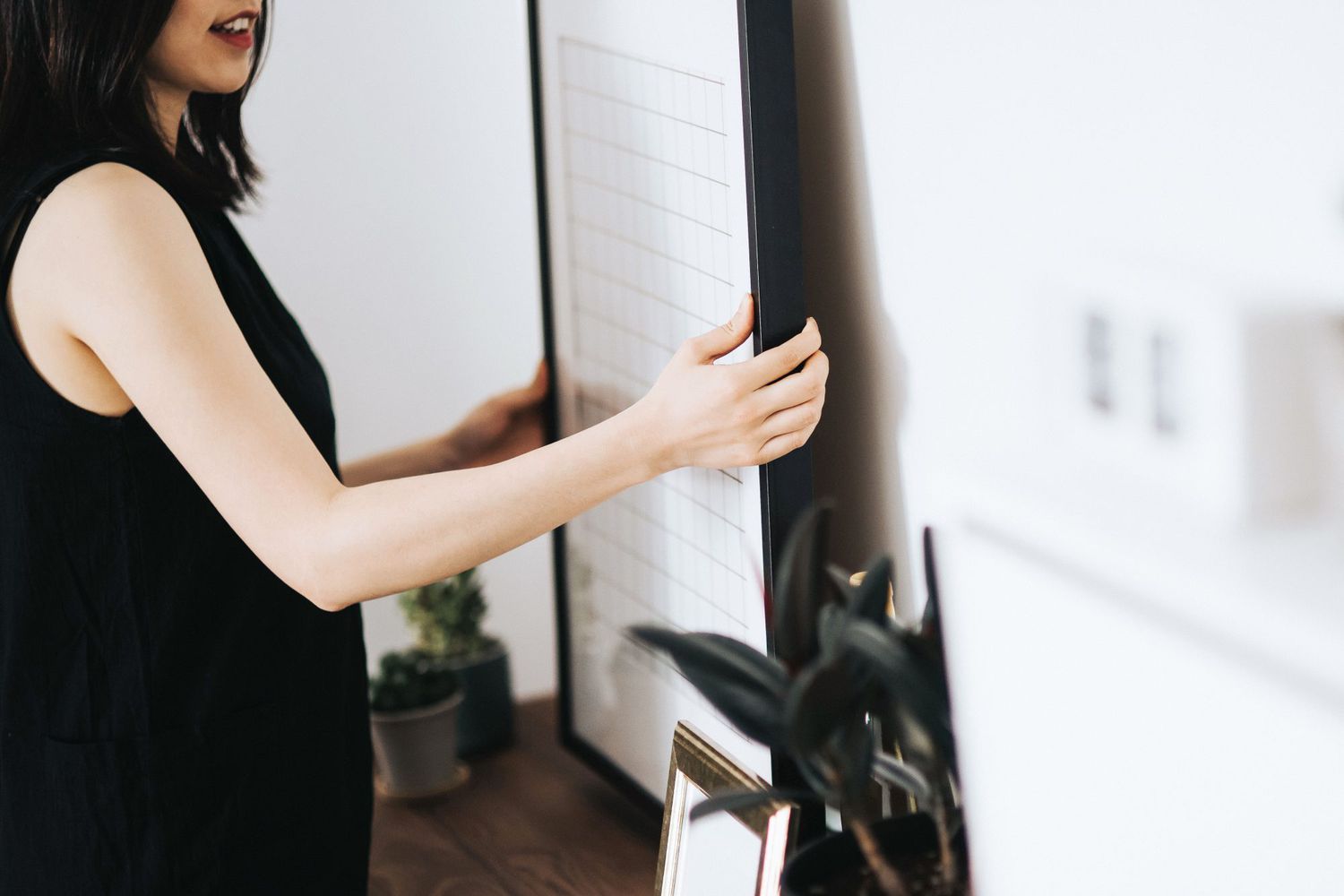 woman hanging framed art to wall