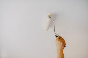 Hand painting a ceiling white with a paint roller.