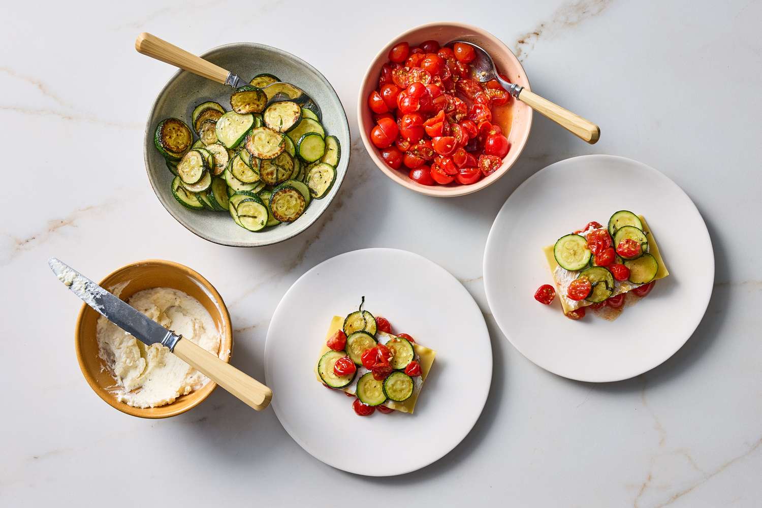 Ingredients and portions of a nobake summer lasagna recipe including ricotta zucchini and tomatoes laid out on plates and bowls
