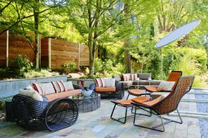 Outdoor patio area with modern furniture and cushions surrounded by trees and greenery