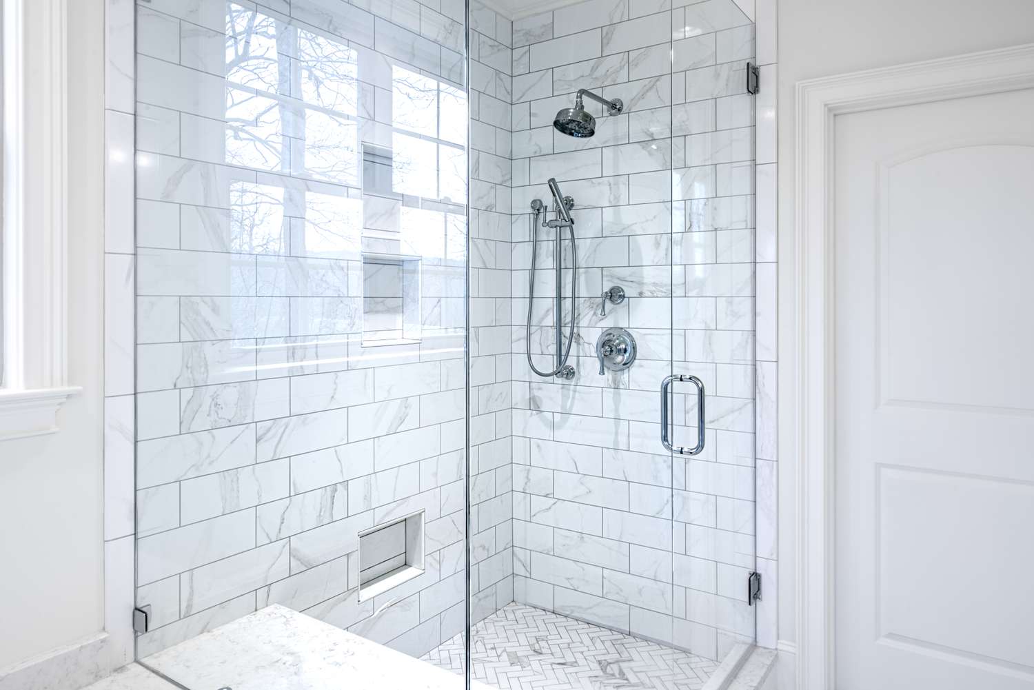 Modern glassenclosed shower with white tile walls and a rainfall showerhead