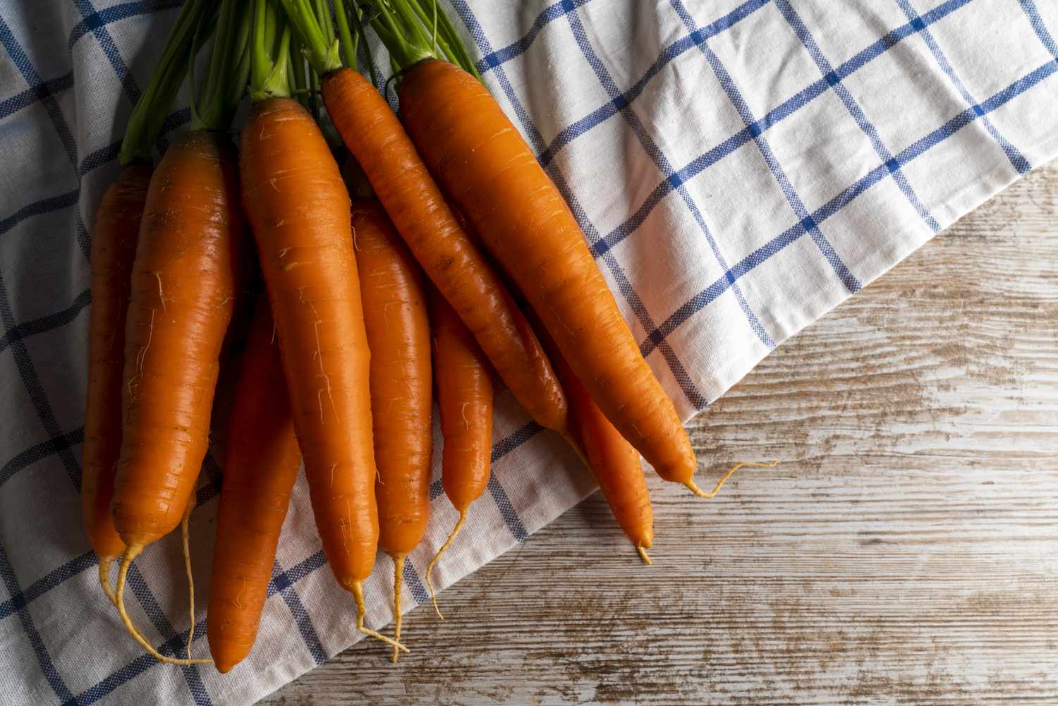 A bunch of carrots placed on a checkered cloth on a wooden surface