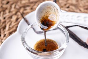 A teaspoon of vanilla bean paste being poured into a small glass bowl