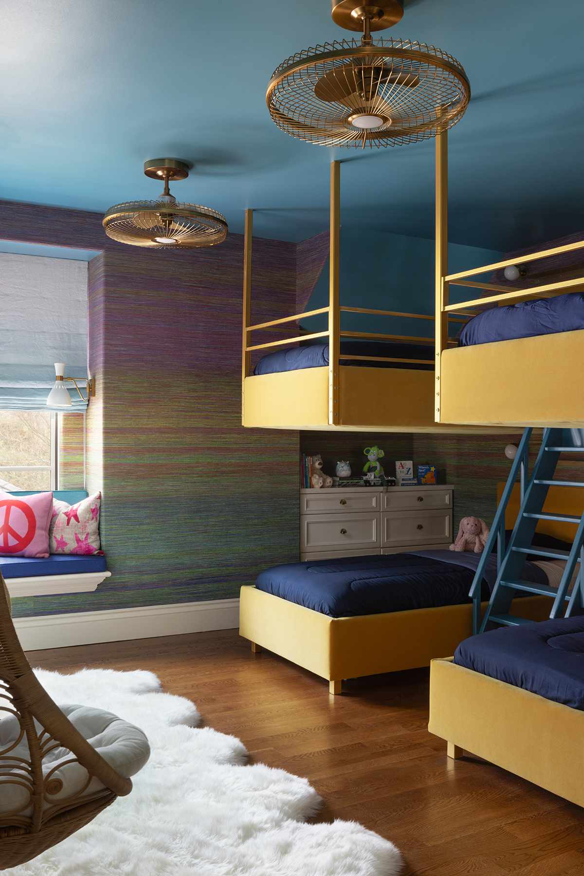 A childrens bunk room with bright yellow bunk beds and rainbow ombre wallpaper. A plush sheepskin rug in the foreground.