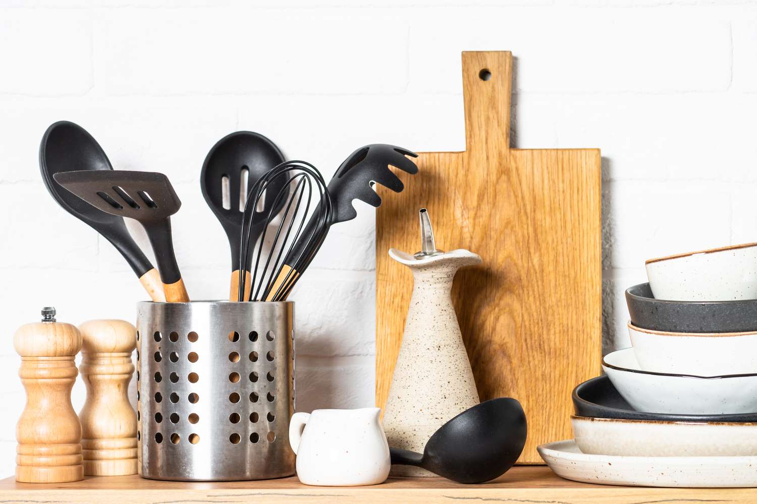 A collection of kitchen utensils in a holder and dishware on a wooden surface