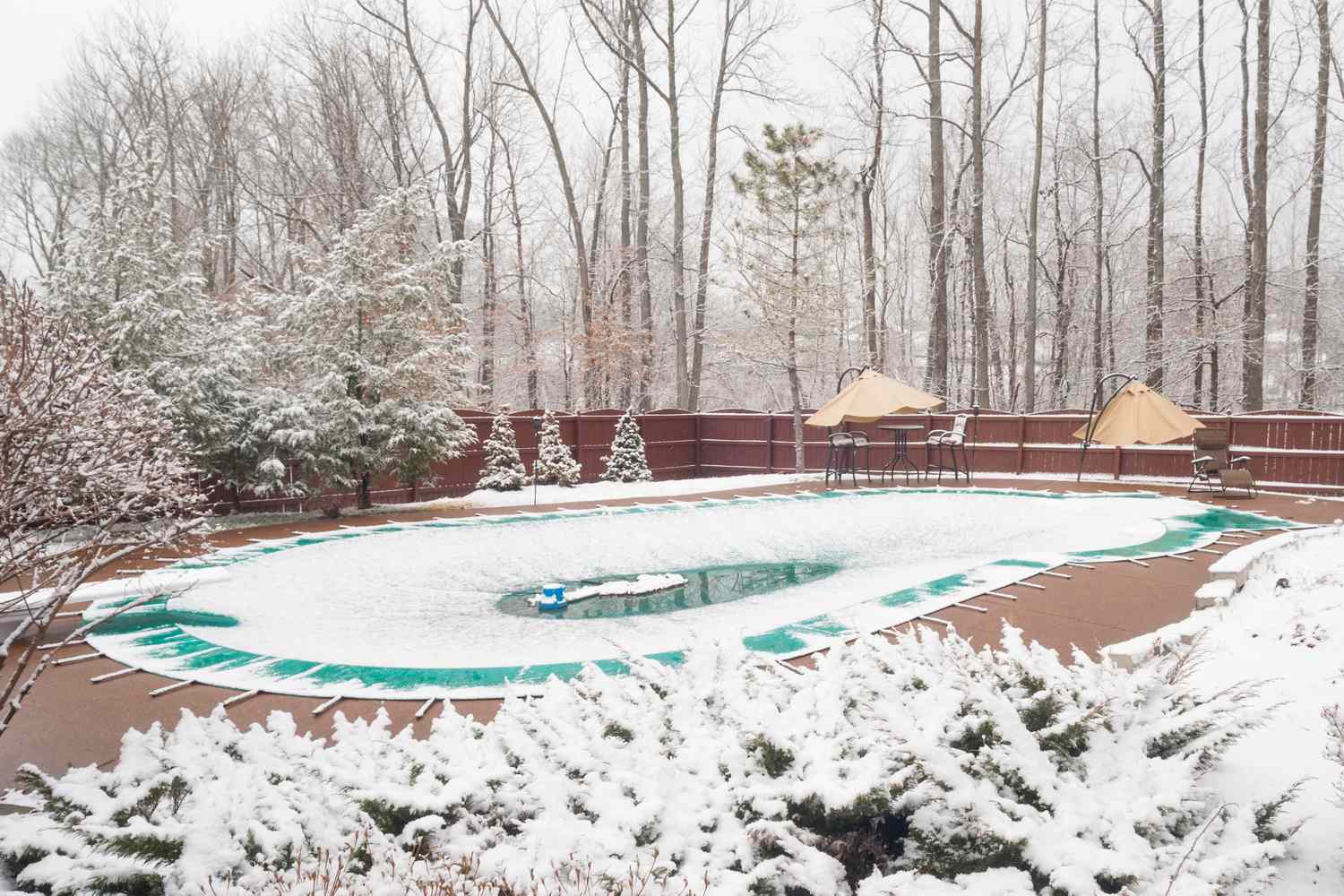 A snowcovered backyard with a pool covered for winter