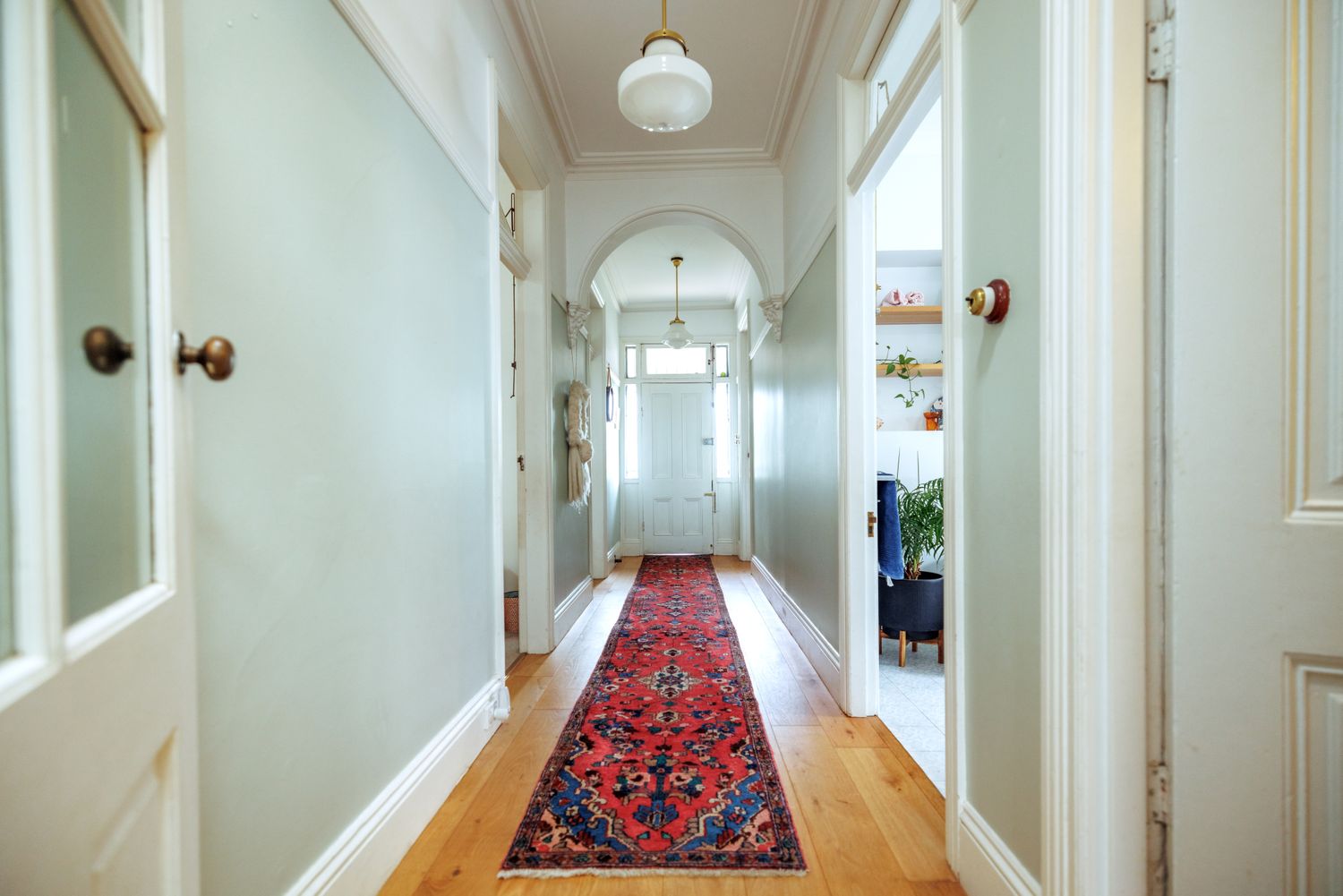 Long entryway with a patterned rug on hardwood flooring view towards a doorway with lighting fixtures overhead
