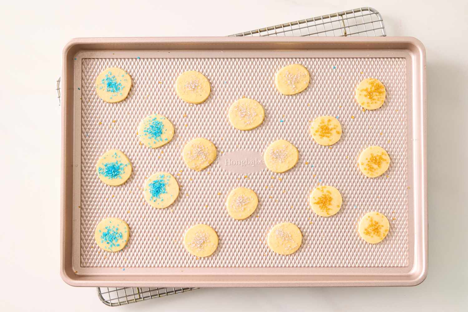 Sheet tray with round baked cookies decorated with sprinkles and sugar cooling on a rack
