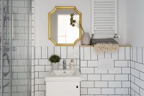 Bathroom with a vanity sink a goldframed mirror and a towel on a shelf above
