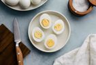 A plate containing four halved hardboiled eggs a knife and cloth napkin nearby