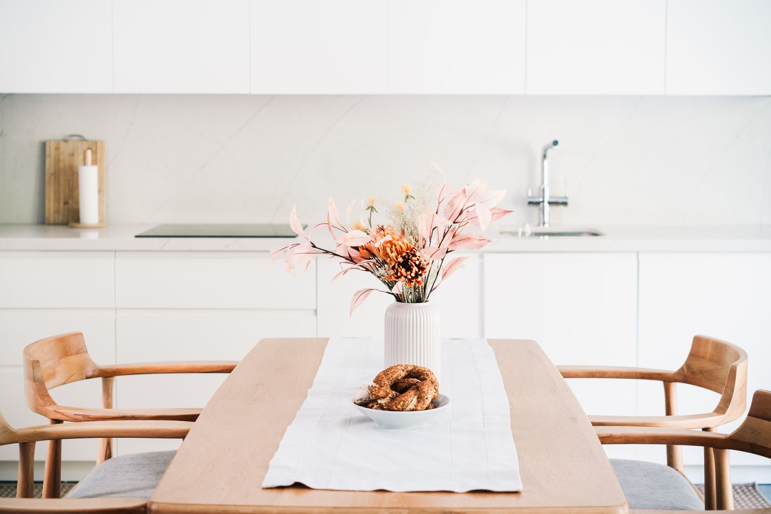 A neatly arranged dining table in a kitchen with a vase of flowers and a dish of pastries