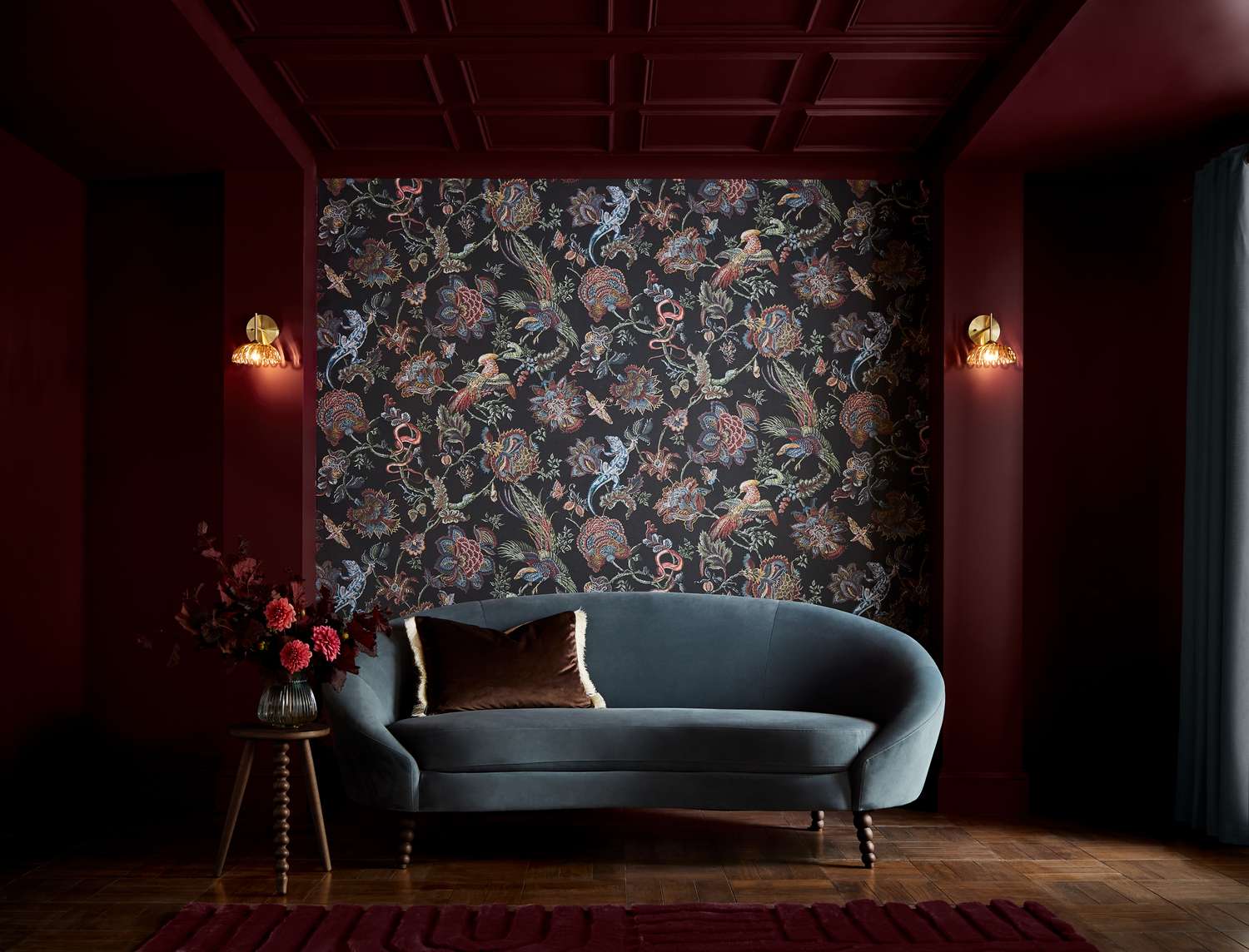 Dark living room with a patterned feature wall velvet sofa side table with flowers and moody lighting