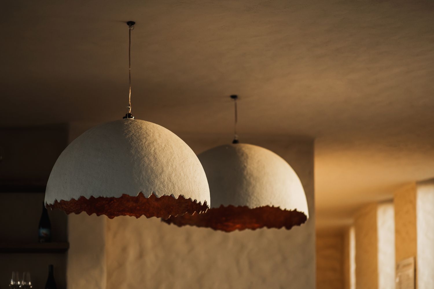 Two domeshaped pendant lights with a textured edge hanging in a softly lit interior