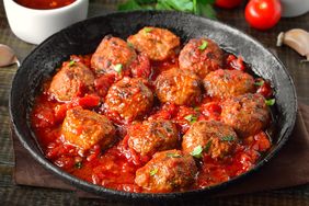A pan of meatballs cooked in red sauce garnished with parsley and surrounded by ingredients like garlic and tomatoes